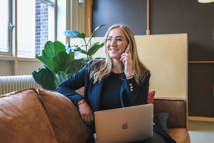 A woman talking on a cell phone while working on a laptop.